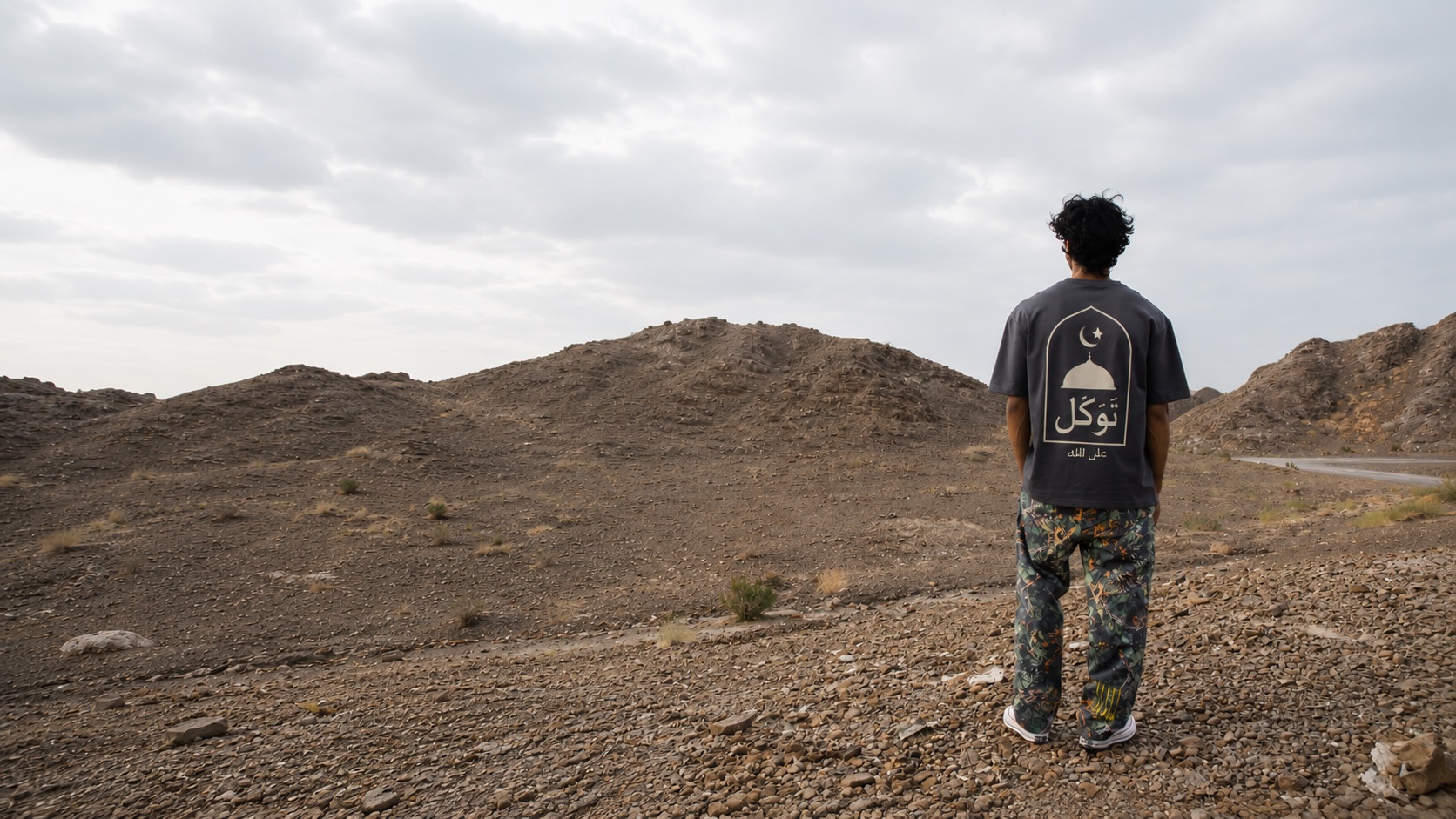 A man walks into the desert wearing the Tawakkul tee, its calligraphy back print facing the horizon